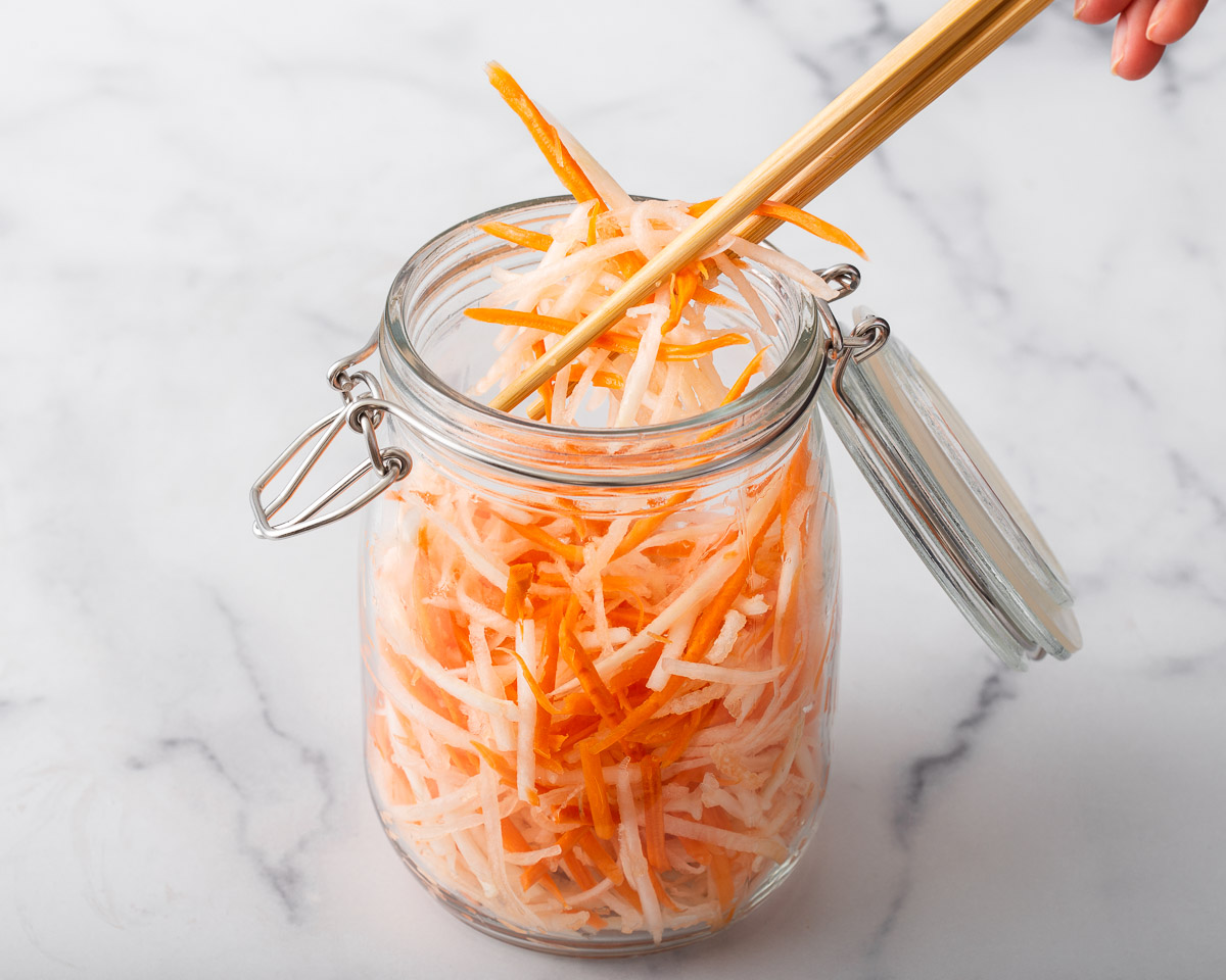 Someone placing shredded carrots and daikon into a mason jar.