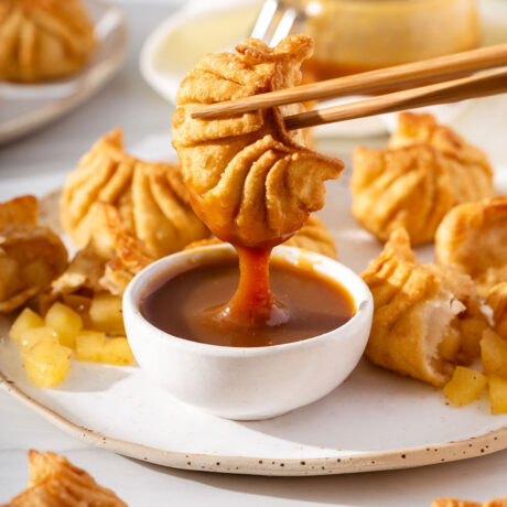 Up close of an apple dumpling being dipped in caramel with chopsticks