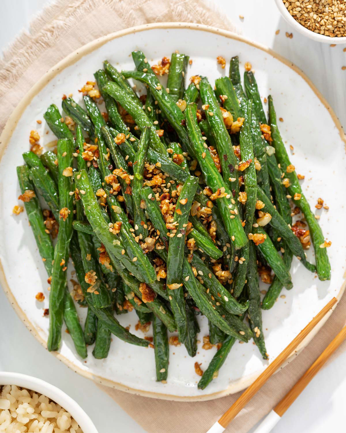 Looking down A plate of garlic green beans with rice and sesame seeds nearby
