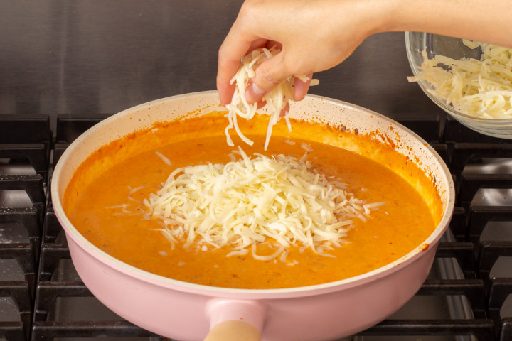 Adding cheese to a pot of flavored kimchi