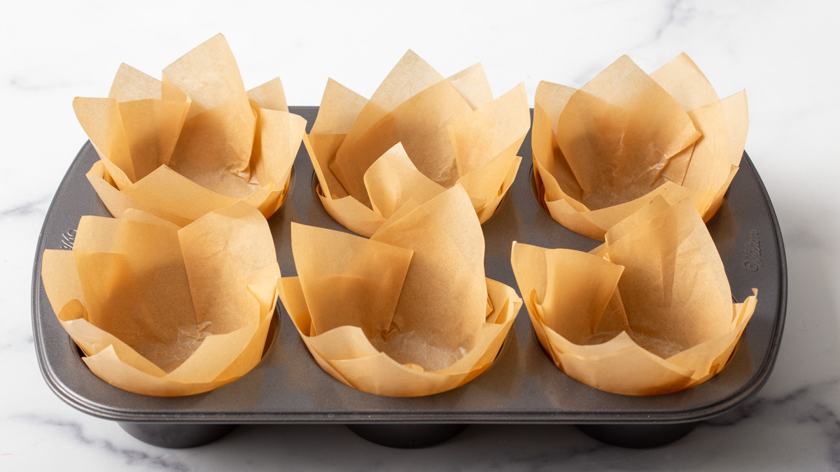 A muffin tin lined with cut parchment paper