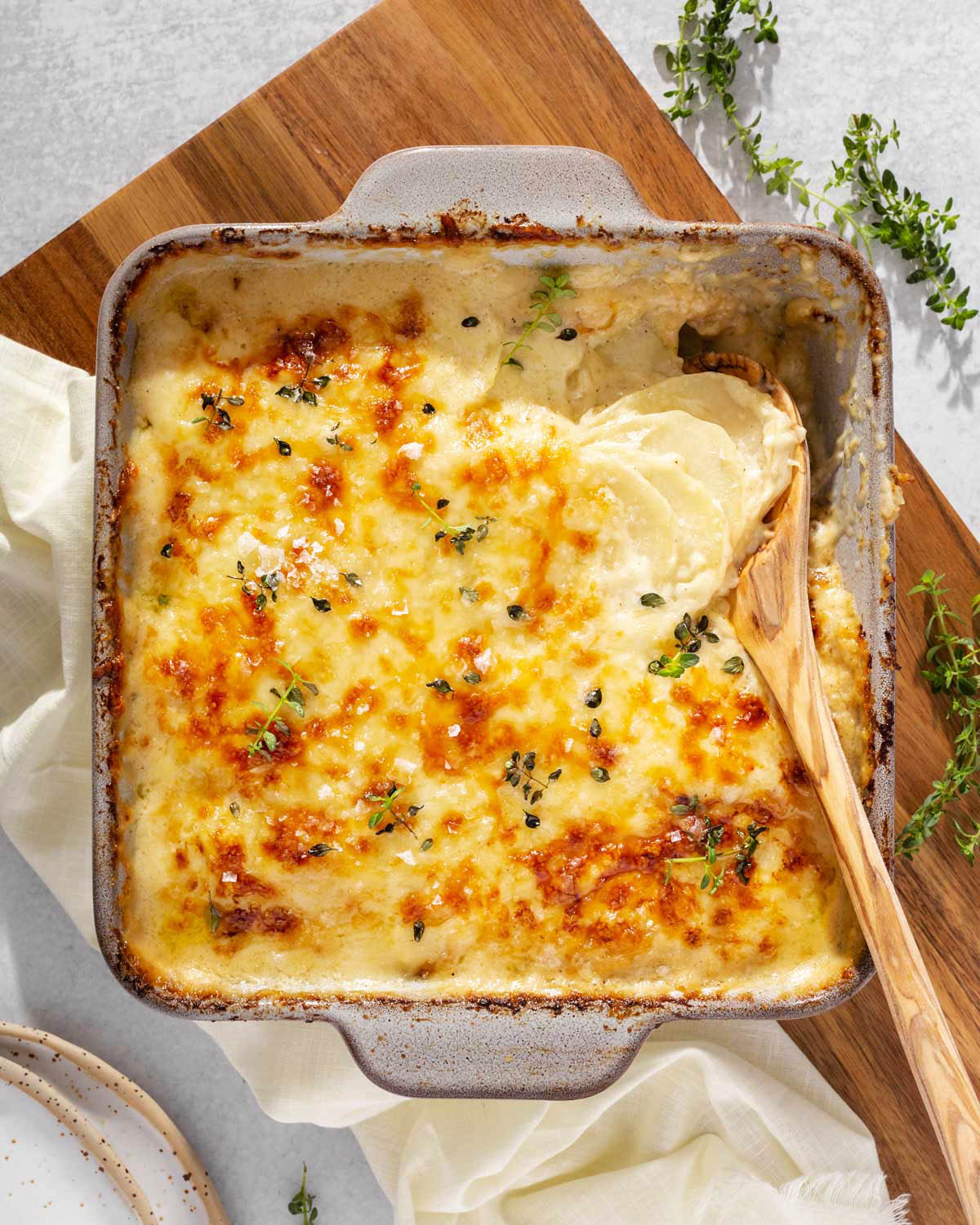 Looking down at a casserole dish full of potato au gratin with a wooden spoon scooping out a serving