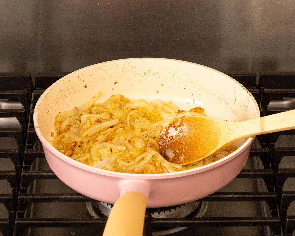 Onions and garlic being caramelized in a deep skillet on the stove