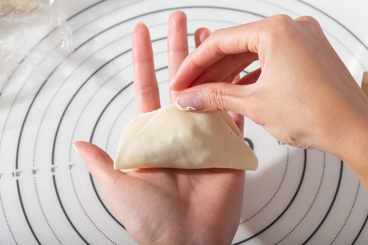 Folding over a dumpling wrapper over its filling