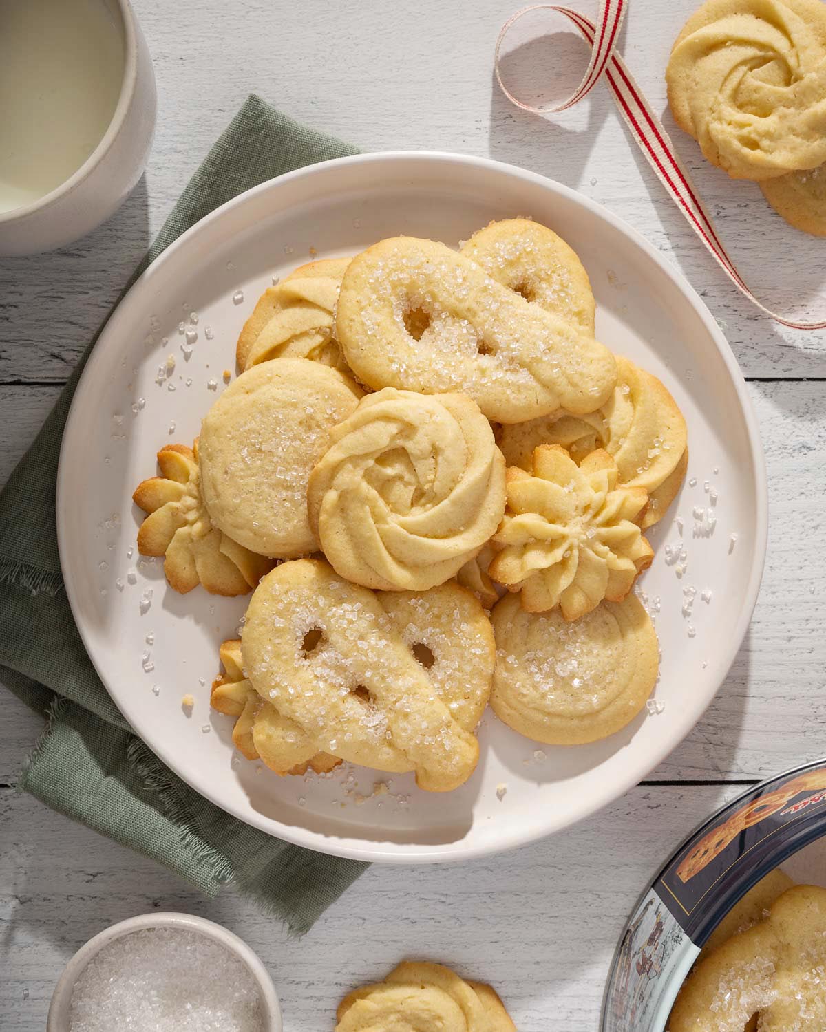 Looking down at a plate piled with danish butter cookies with the tin and more cookies nearby.