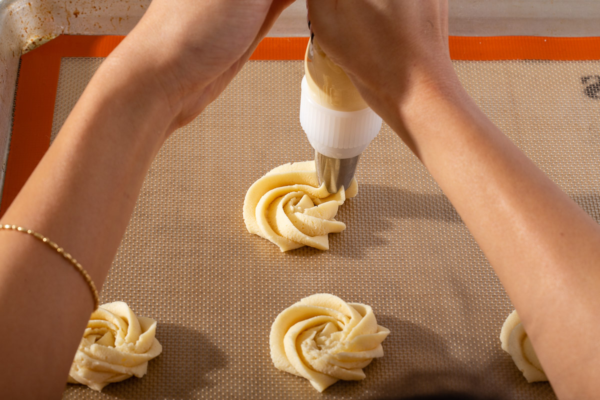 Piping cookie dough onto a slip mat lined baking tray with a star tipped icing tip.