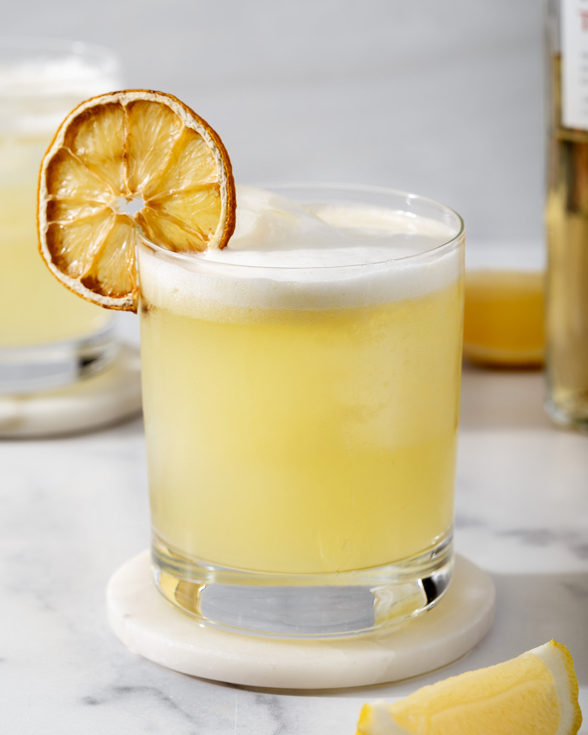 A Japanese yuzu whiskey sour in a rocks glass on a coaster.