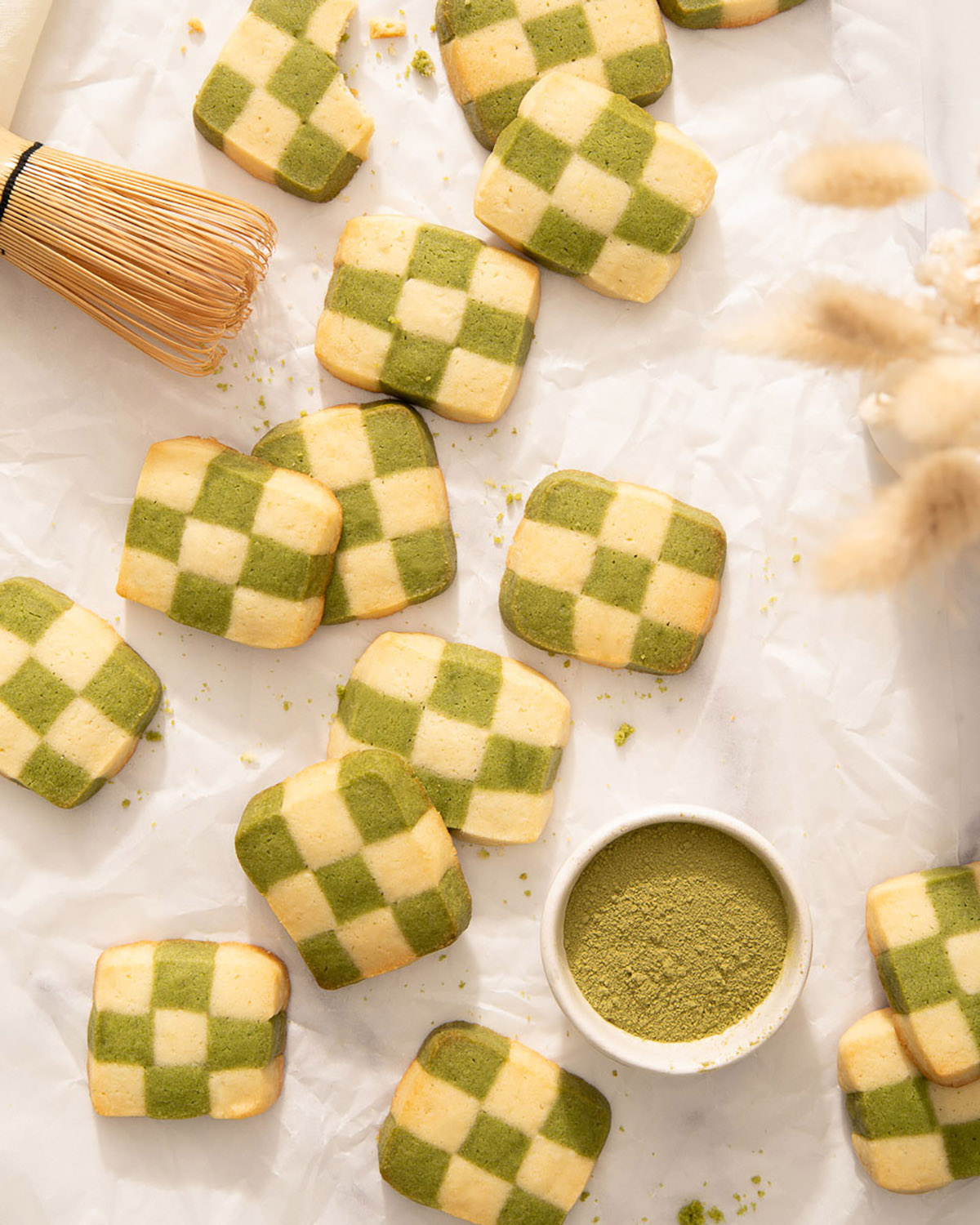 Looking down at checkerboard cookies and matcha powder on a sheet of parchment paper