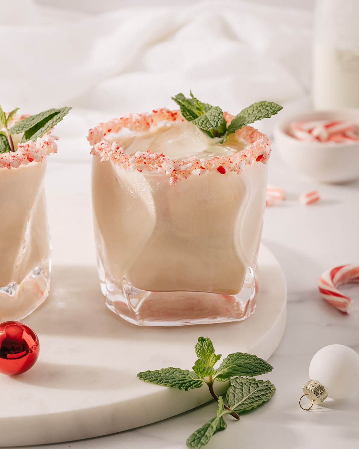 Two glasses of holiday white russians on a marble serving tray with candy canes nearby.