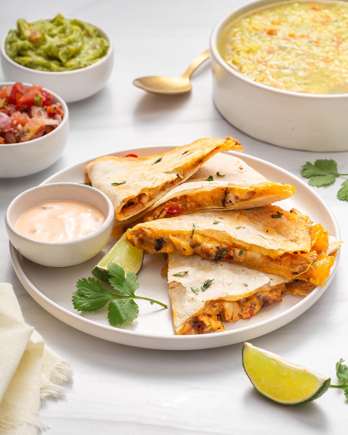 A plate of chicken quesadillas with soup next to it