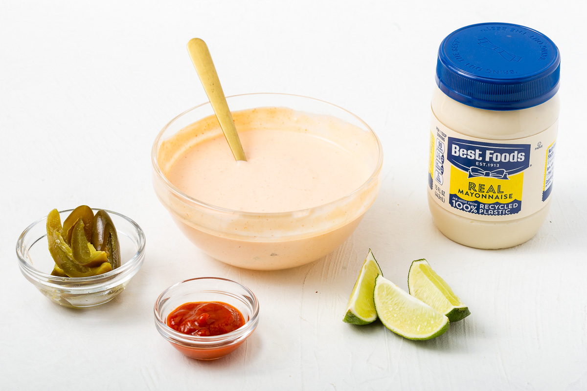 Sriracha mayo in a glass bowl surrounded by the ingredients to make it.