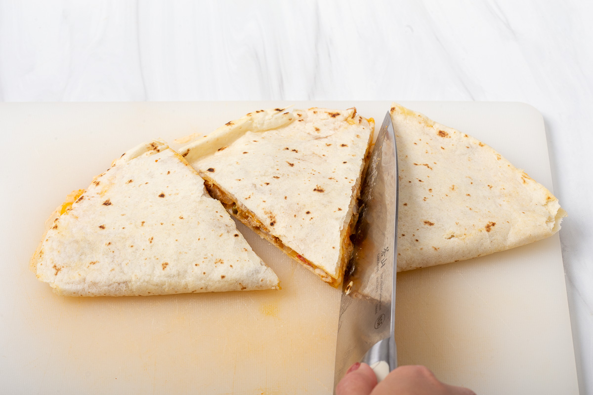 Someone slicing the completed quesadilla into three portions.