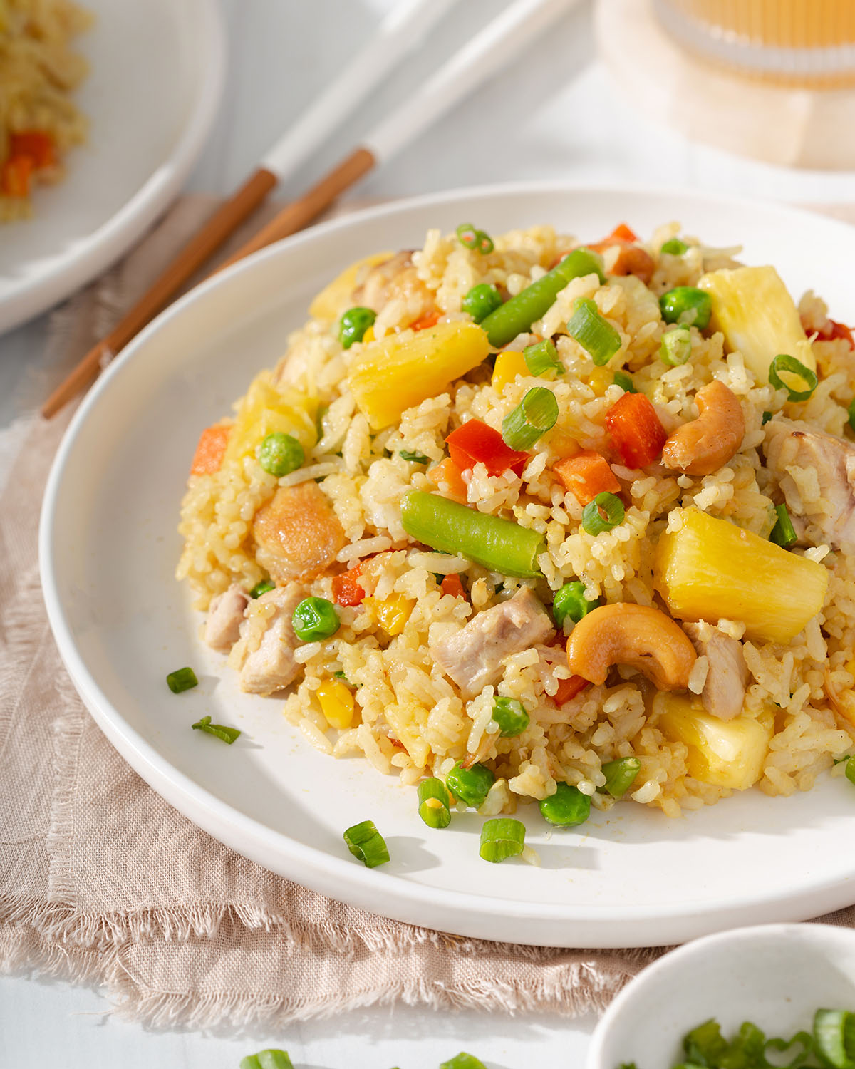 A 3/4 view of pineapple fried rice sitting on a plate with table settings nearby.