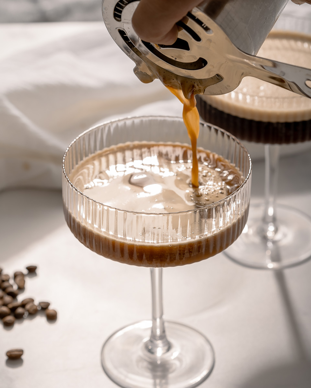 Pouring a mixed espresso martini into a glass from a metal shaker and strainer