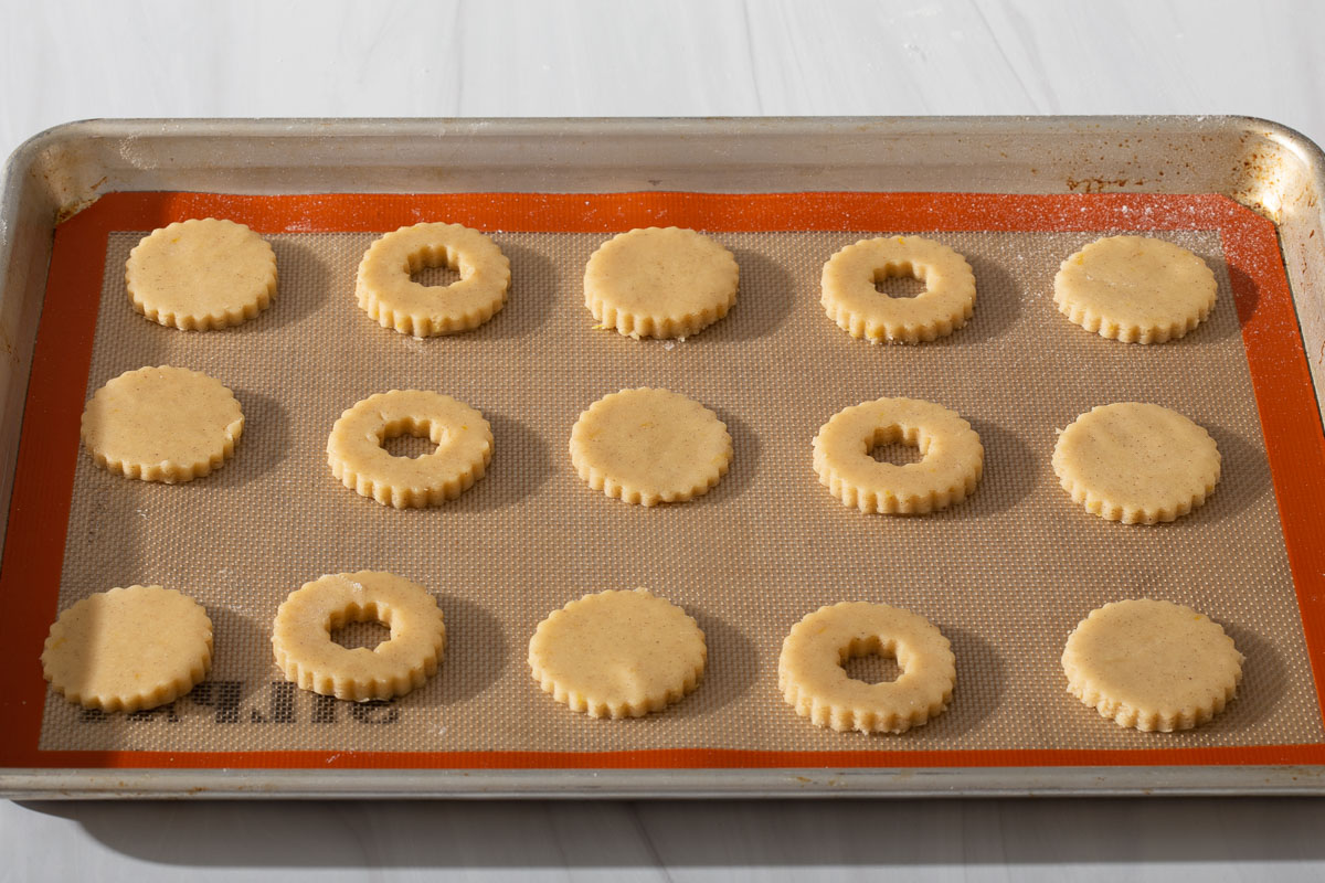 A baking tray full of cut out cookie tops and bottoms on a slipmat