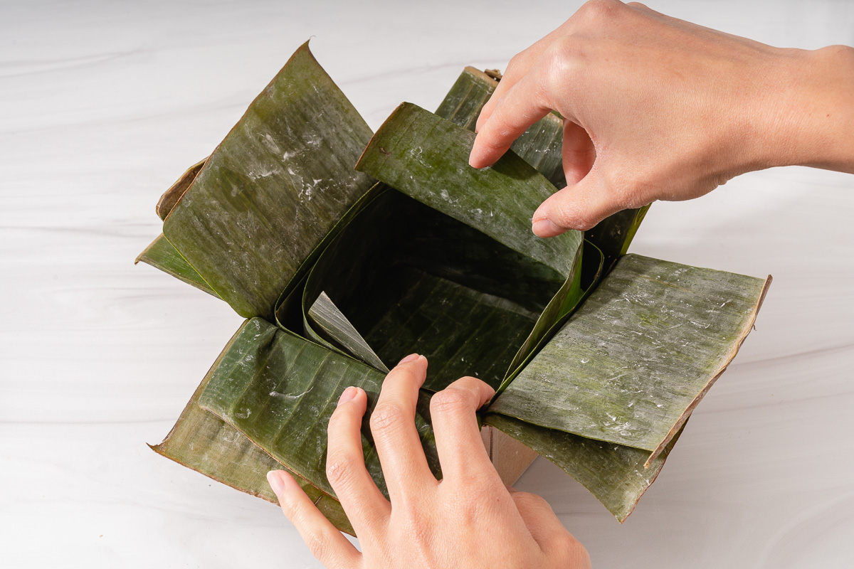 Lining the inside corners of the mold with thin strips of banana leaves to seal the corners.
