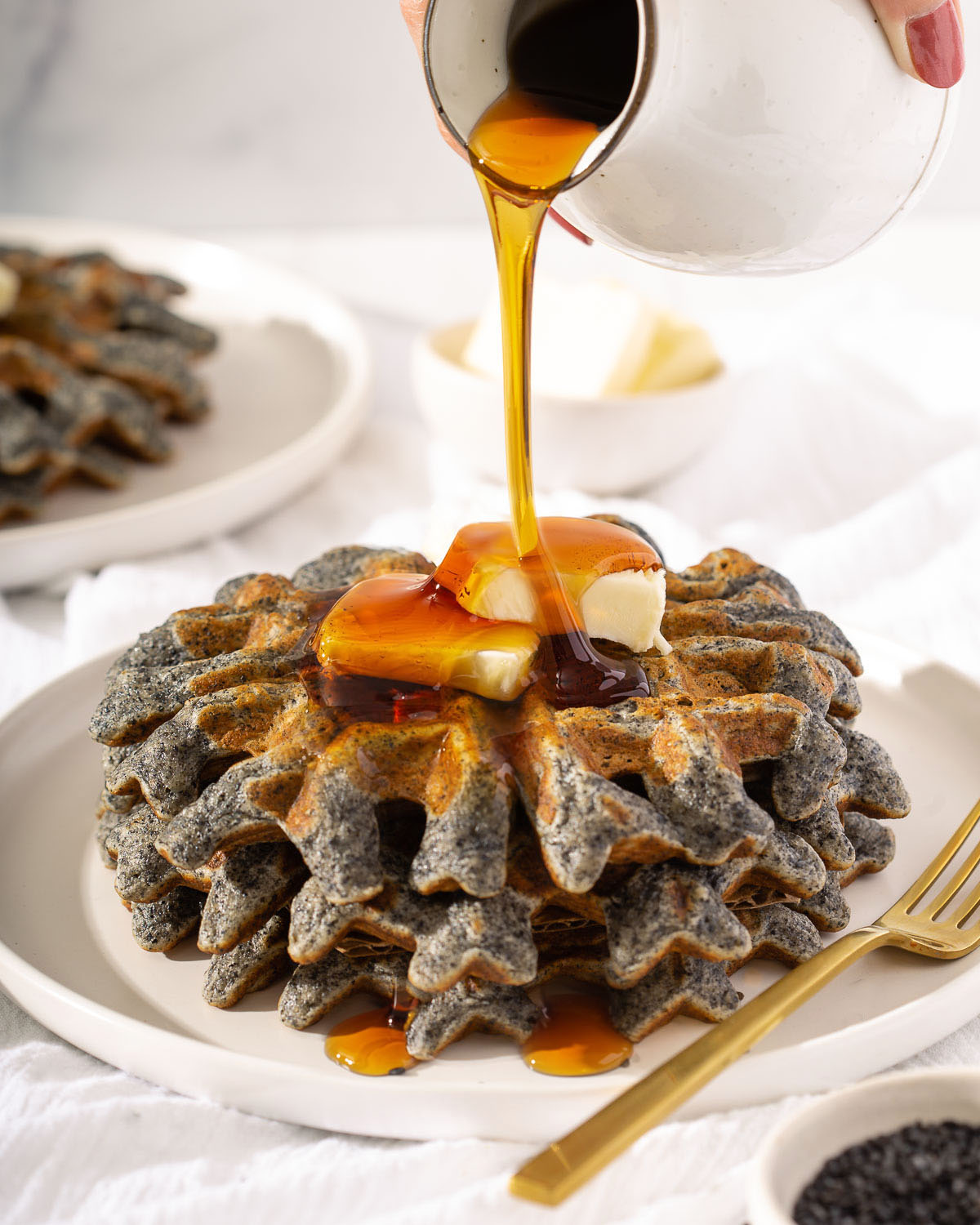 Pouring syrup on to a stack of black sesame waffles topped with butter.