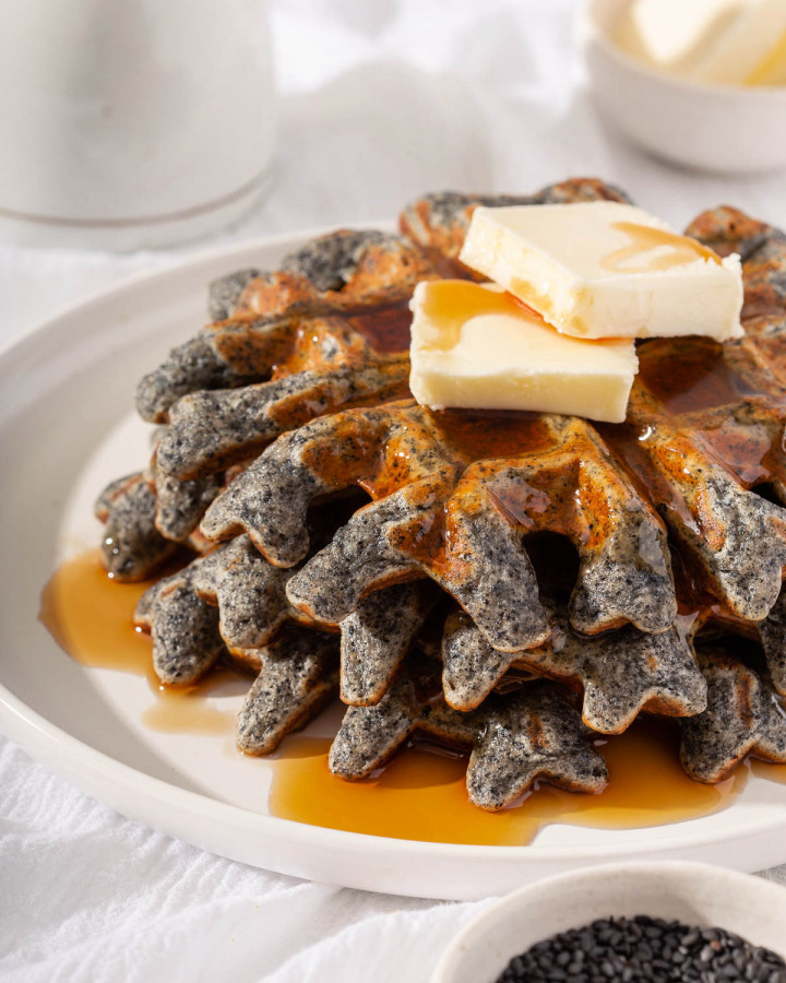 Up close of a stack of sesame waffles topped with syrup and butter.