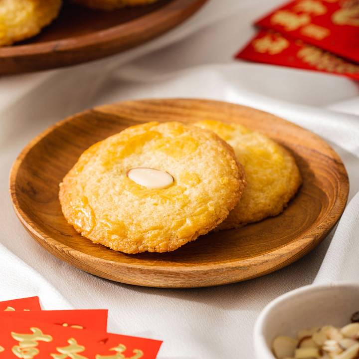 Two easy to make Chinese almond cookies on a plate with Lunar New Year decoration nearby.