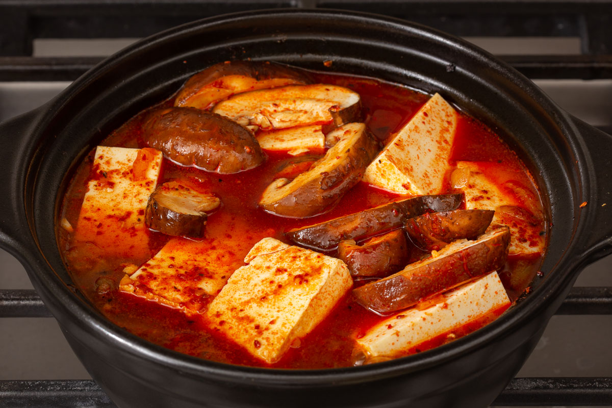 Sliced mushrooms added into the simmering spicy Korean tofu soup.