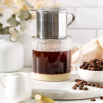 A phin sitting ontop of a glass making Vietnamese coffee.