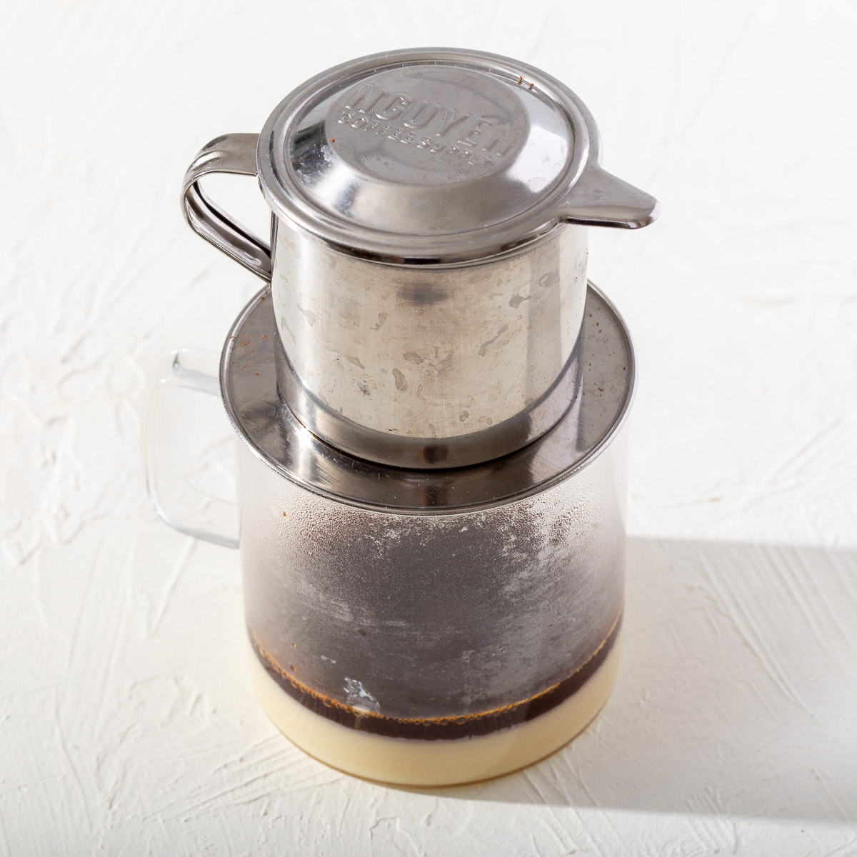 A phin dripping into a glass with condensed milk inside.