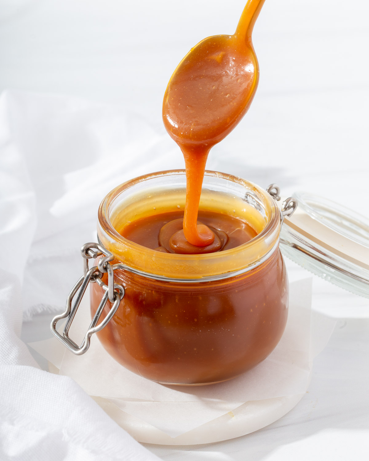 Lifting a spoon dripping with miso caramel sauce from a small glass jar.