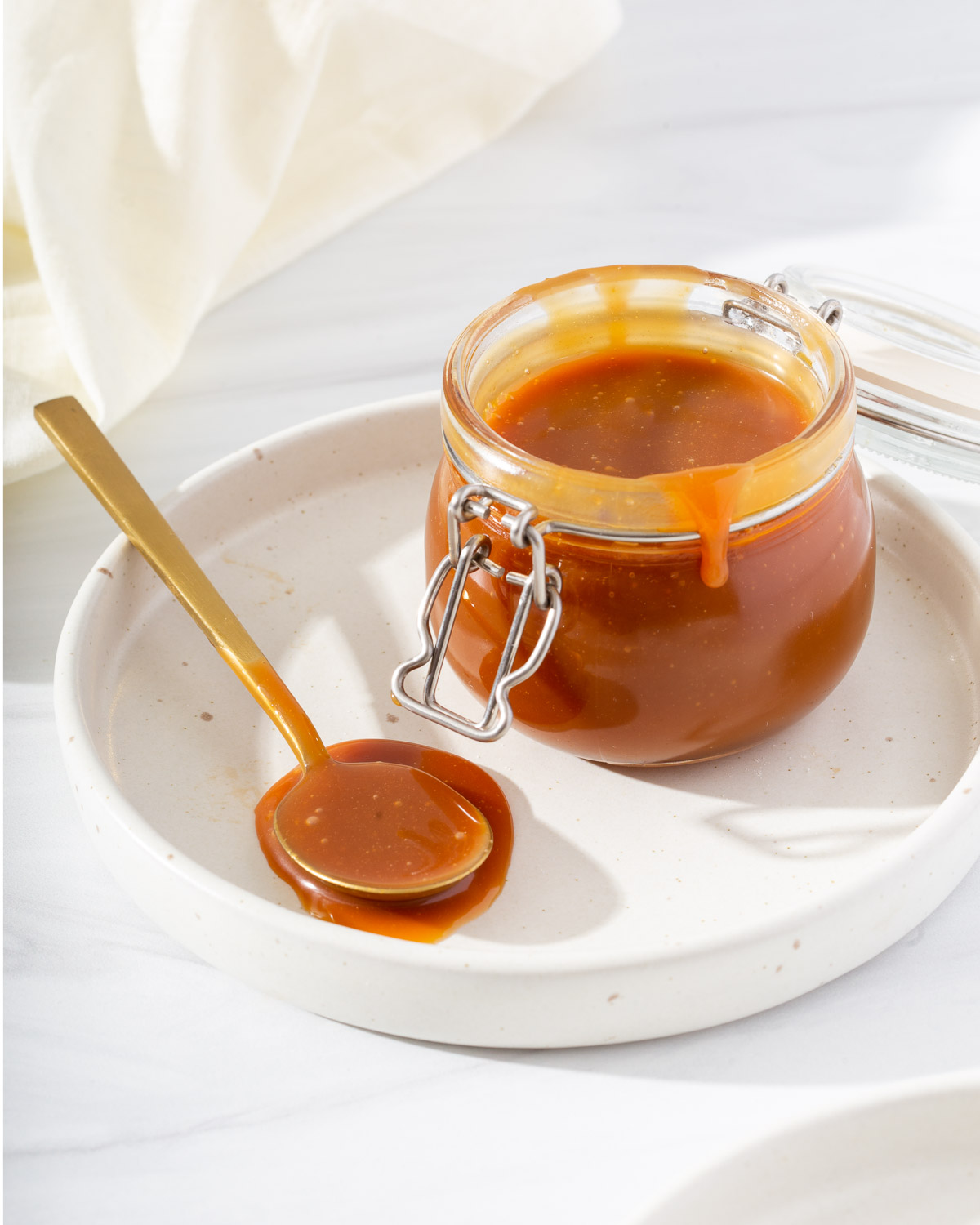 A jar of caramel sauce and spoon on small serving plate.