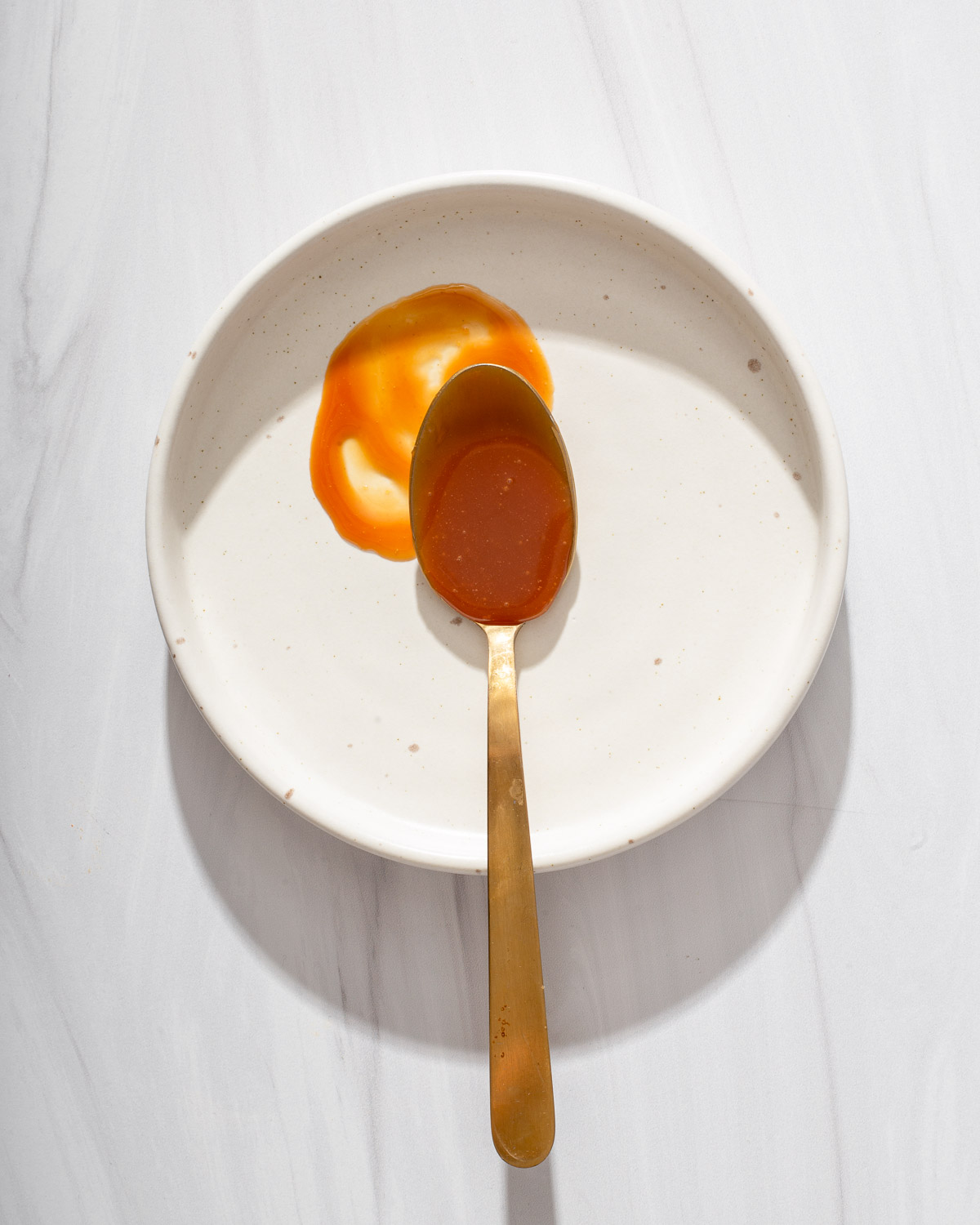 A messy spoon covered with caramel sauce on a plate.