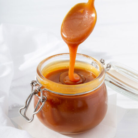 Up close of a spoon dripping caramel into a small glass jar of caramel