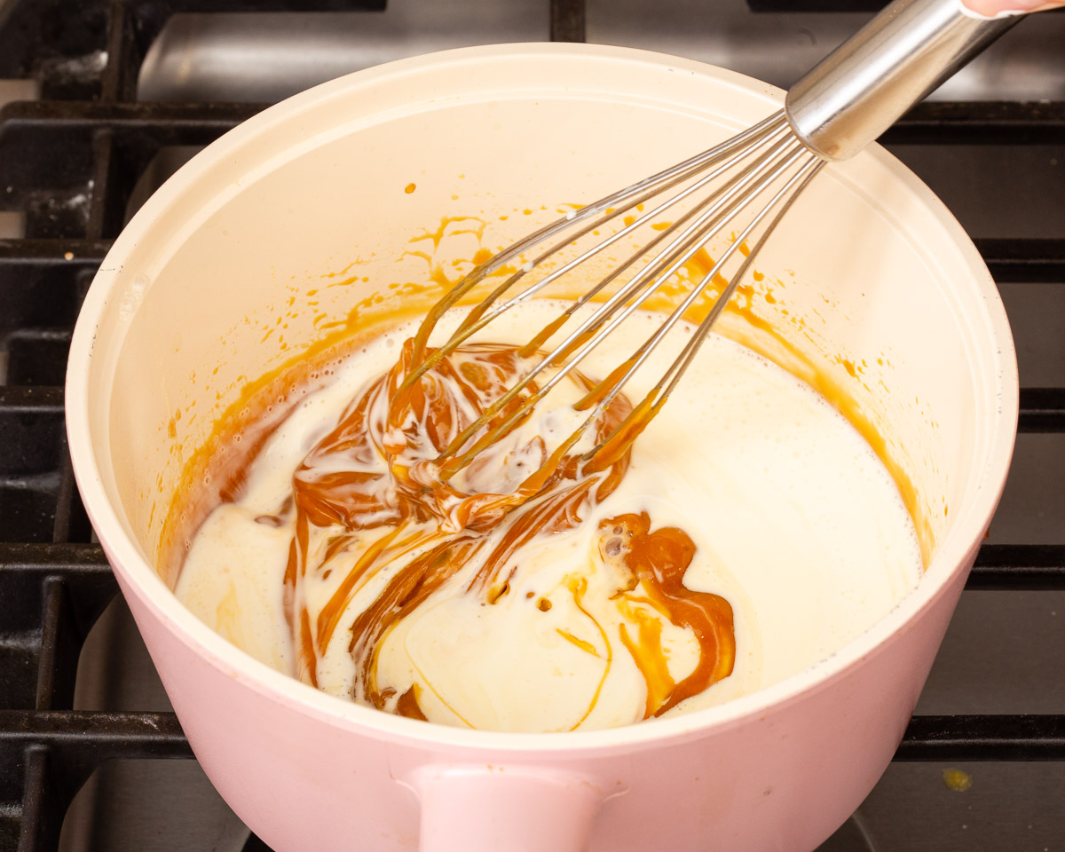 A whisk mixing heavy cream into the caramel to turn it into a sauce.