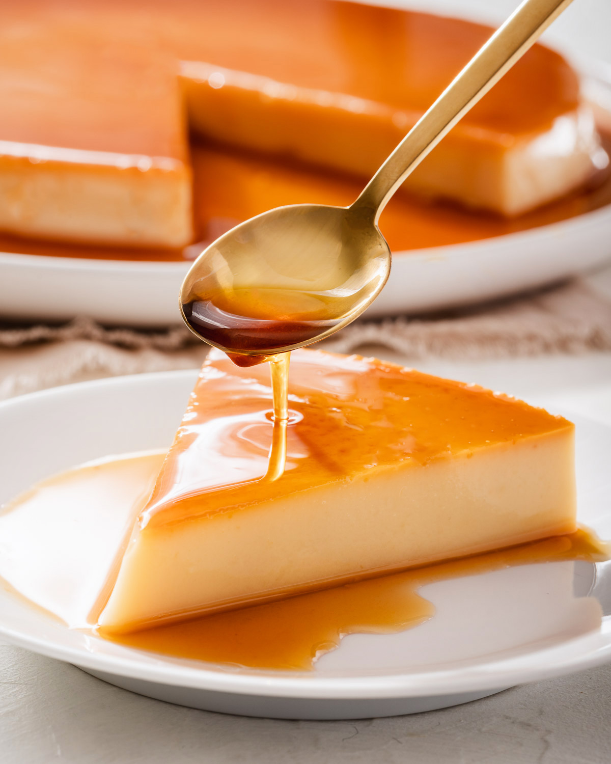 A slice of flan being drizzled with creme caramel on a small plate.