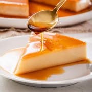 A slice of Vietnamese creme caramel flan on a plate being drizzled with it's caramel sauce.