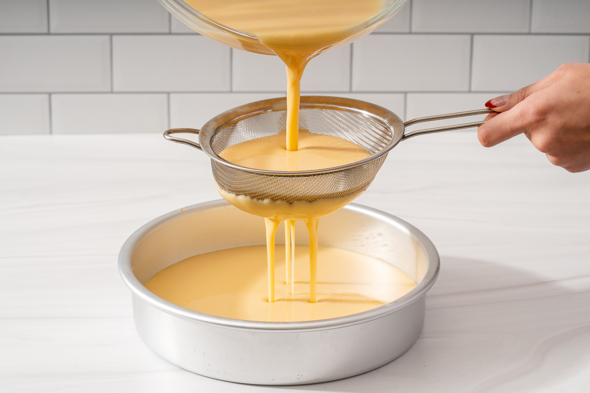 Straining the flan creme through a metal sieve to ensure it is silky smooth.