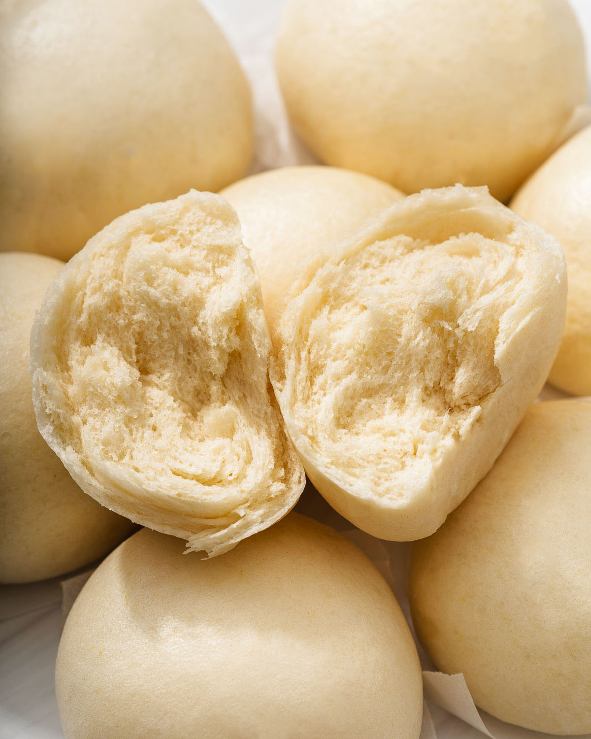 A torn open mantou Chinese steamed bun resting on top of other buns.