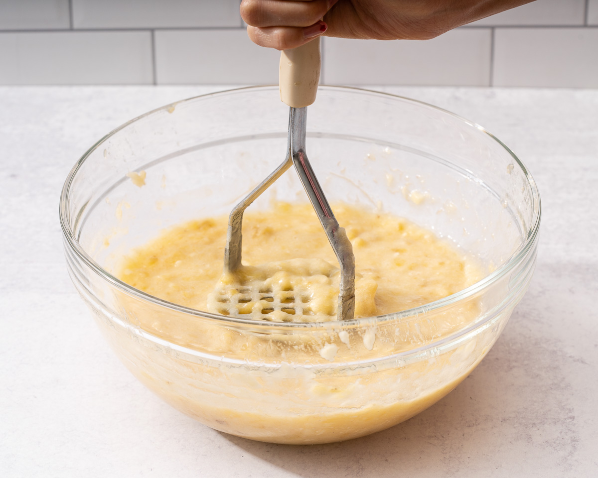 Mashing the overly ripe bananas into a mushy liquid-like consistency.