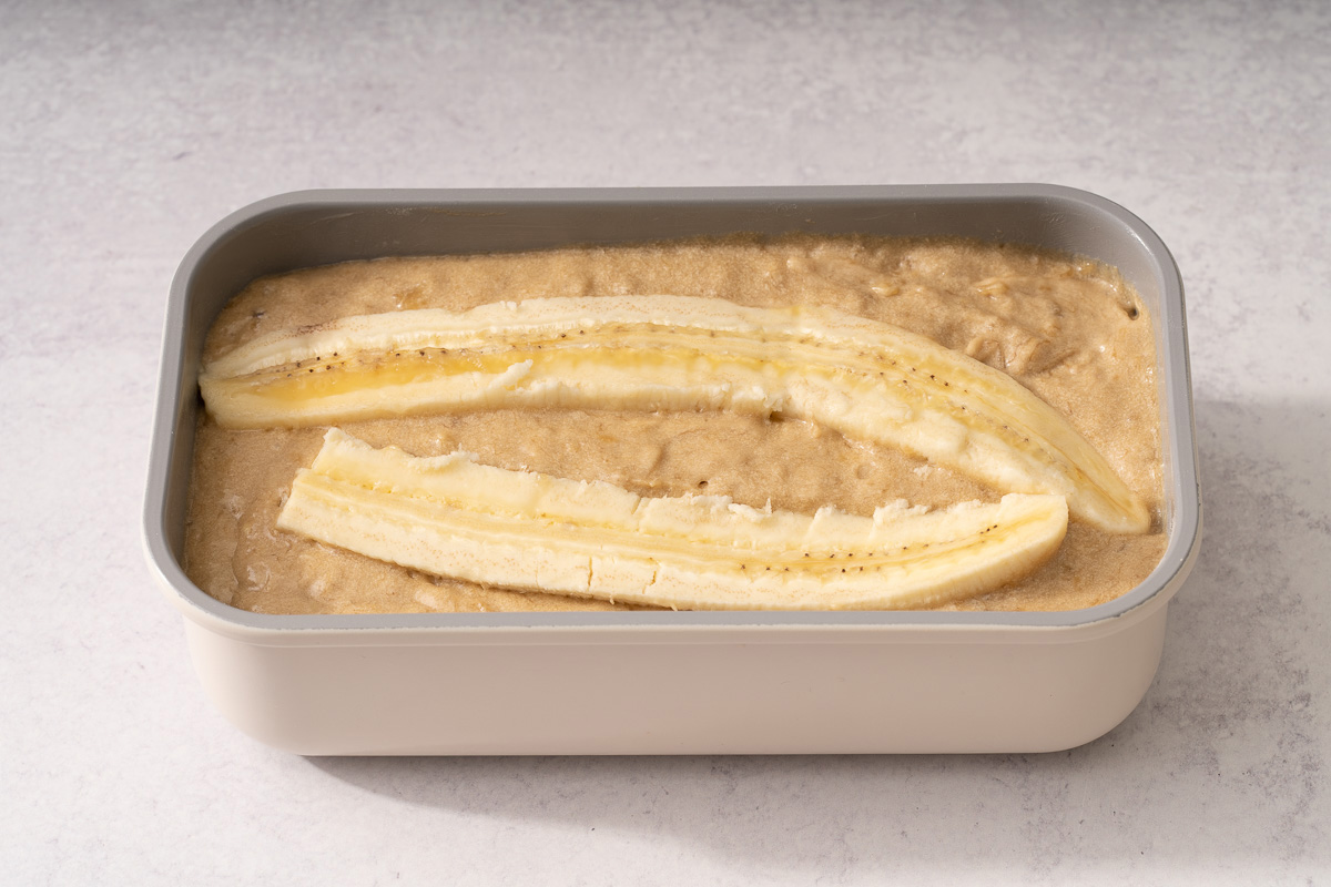 A bread pan filled with the batter and topped with sliced bananas.