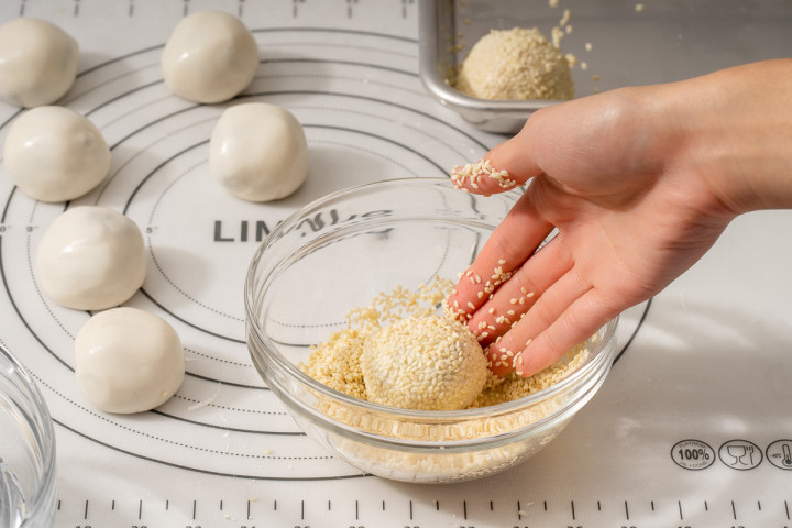 Tossing the filled ball in water then coating in raw sesame seeds.