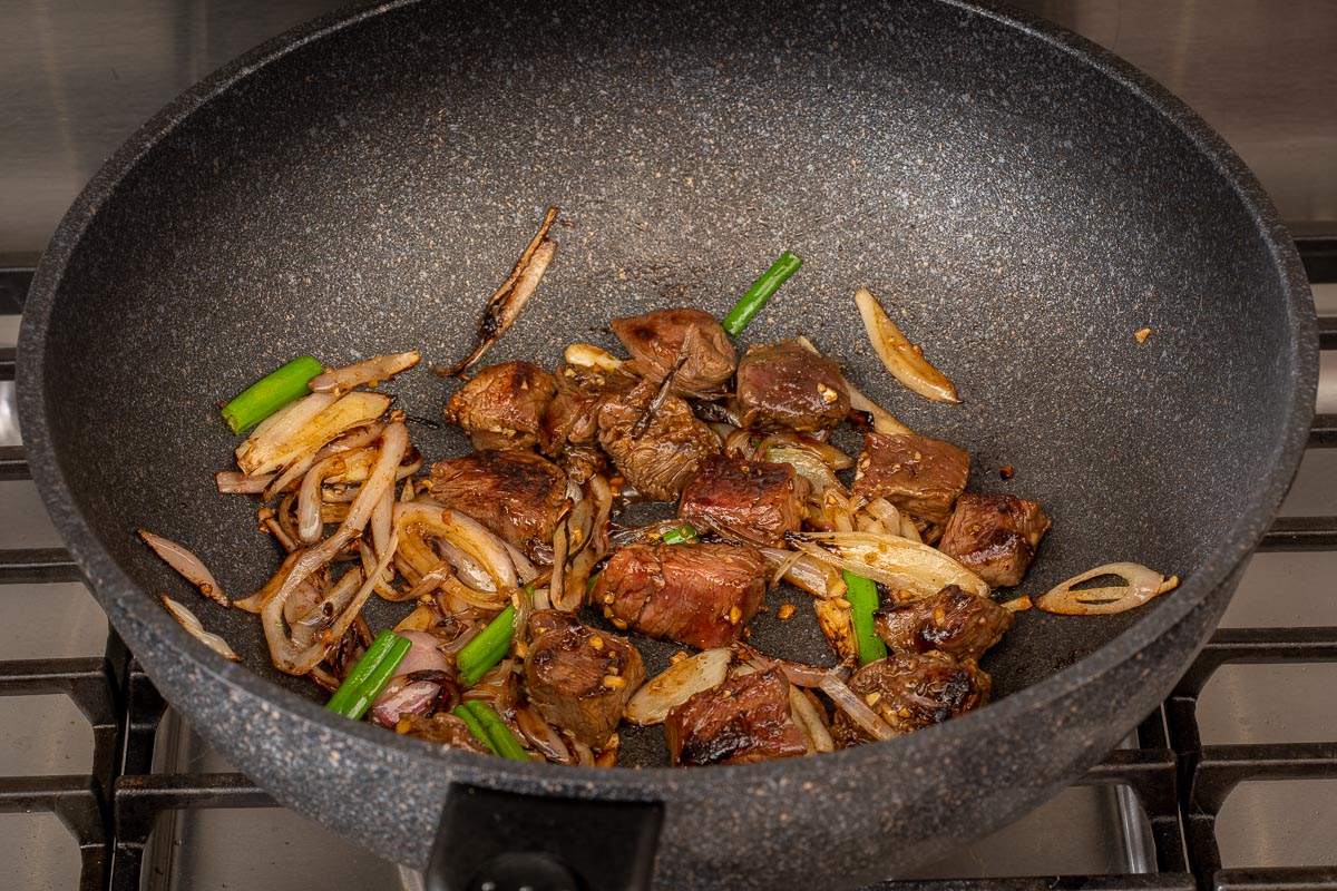 Shallots, green onion, and filet mignon inside a large wok cooking.