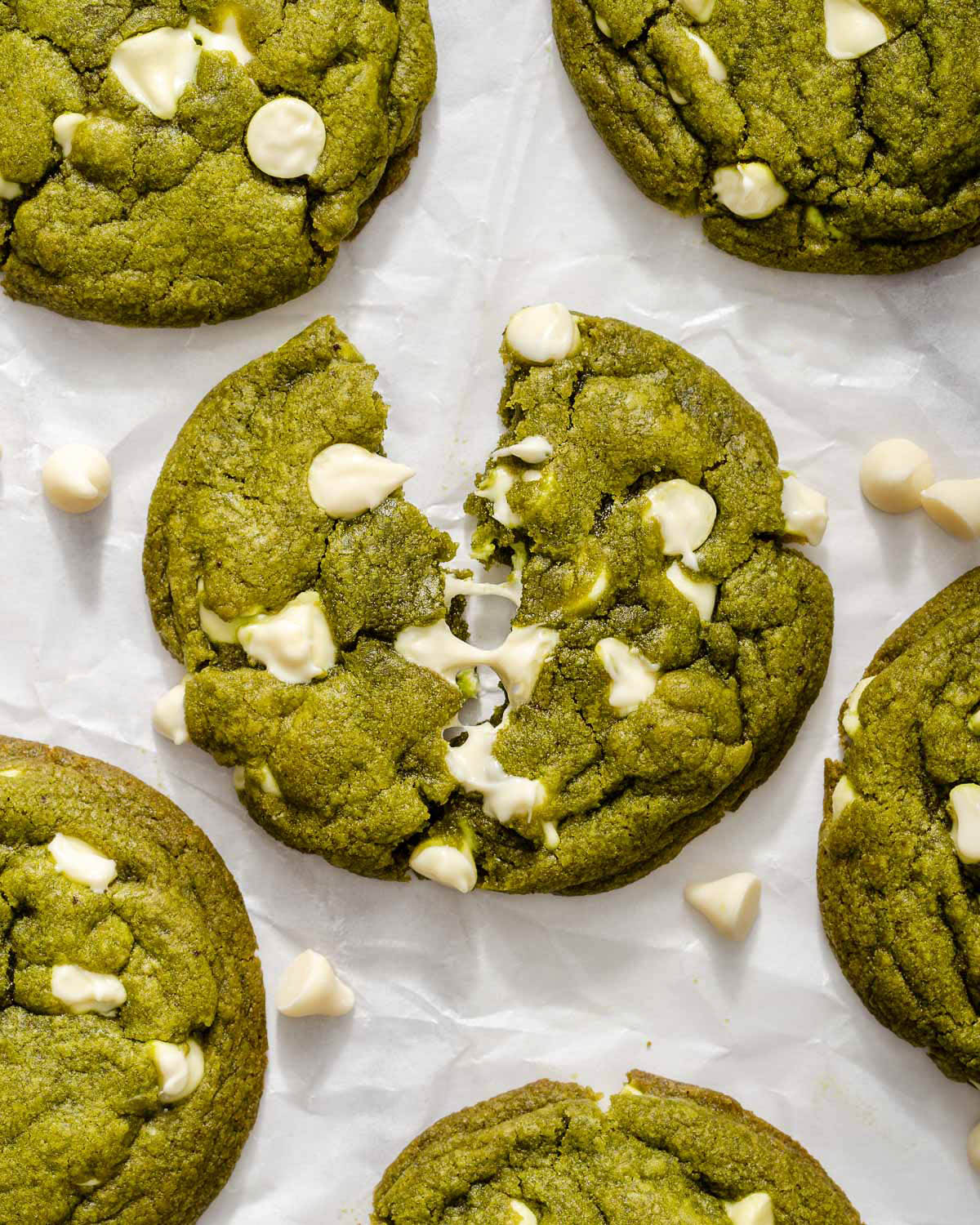 A white chocolate chip matcha cookie slightly torn open to show the gooey white chocolate.