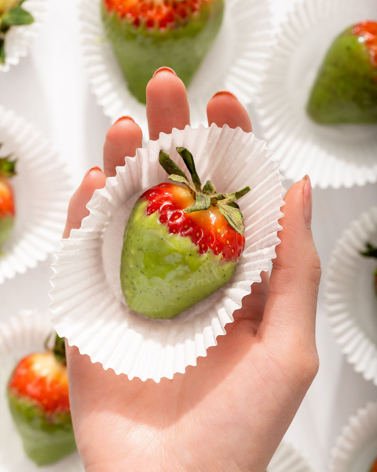 Someone holding a matcha chocolate dipped strawberry in a cupcake wrapper.