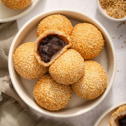Looking down at a bowl of fried sesame balls with an open one showing the red bean paste inside.