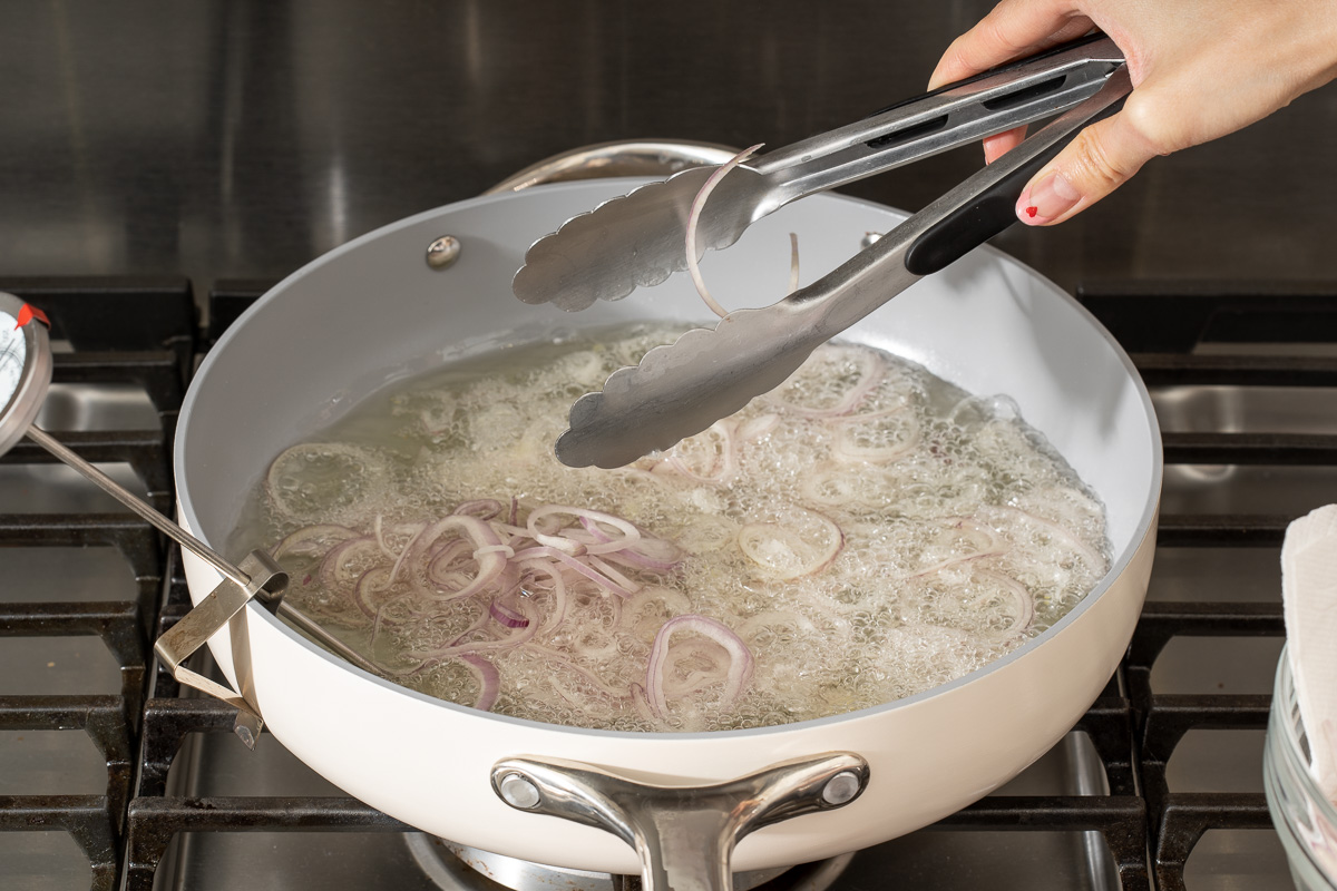 Placing thinly sliced shallots into a deep pan with oil to fry them into crisp.