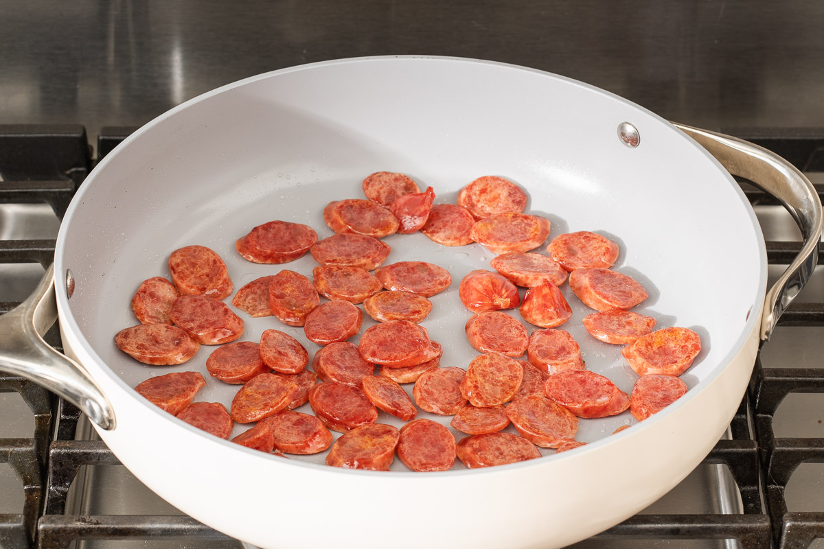 Thinly sliced Chinese sausage cooking in a pan.