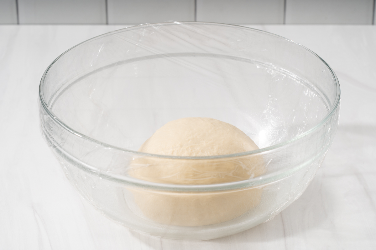 A ball of dough in a covered glass bowl ready to proof.