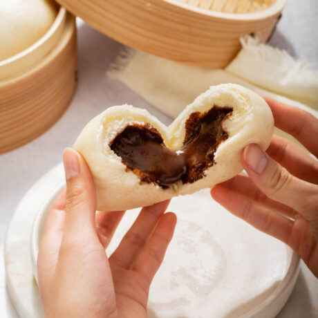 Up close of two hands tearing open a bun filled with melted chocolate.