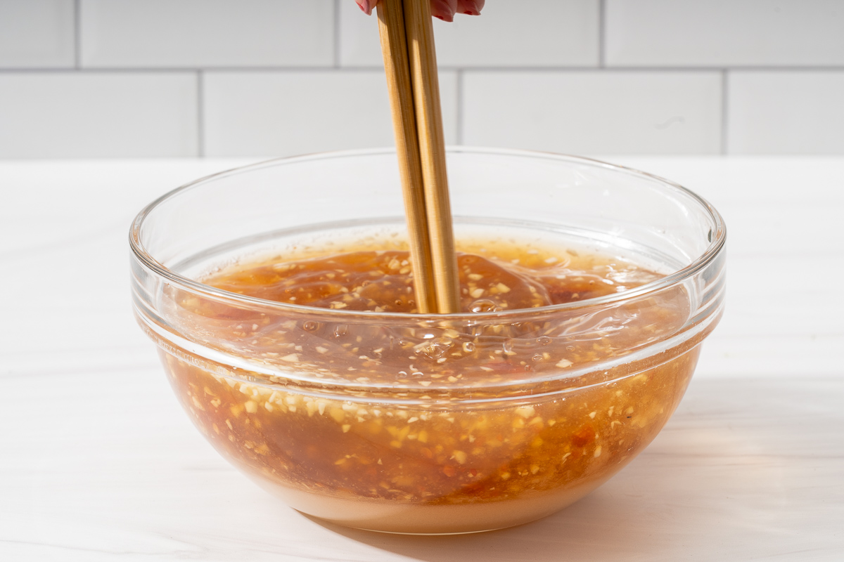 Mixing together a bowl of Vietnamese dipping sauce in a glass bowl with chopsticks.