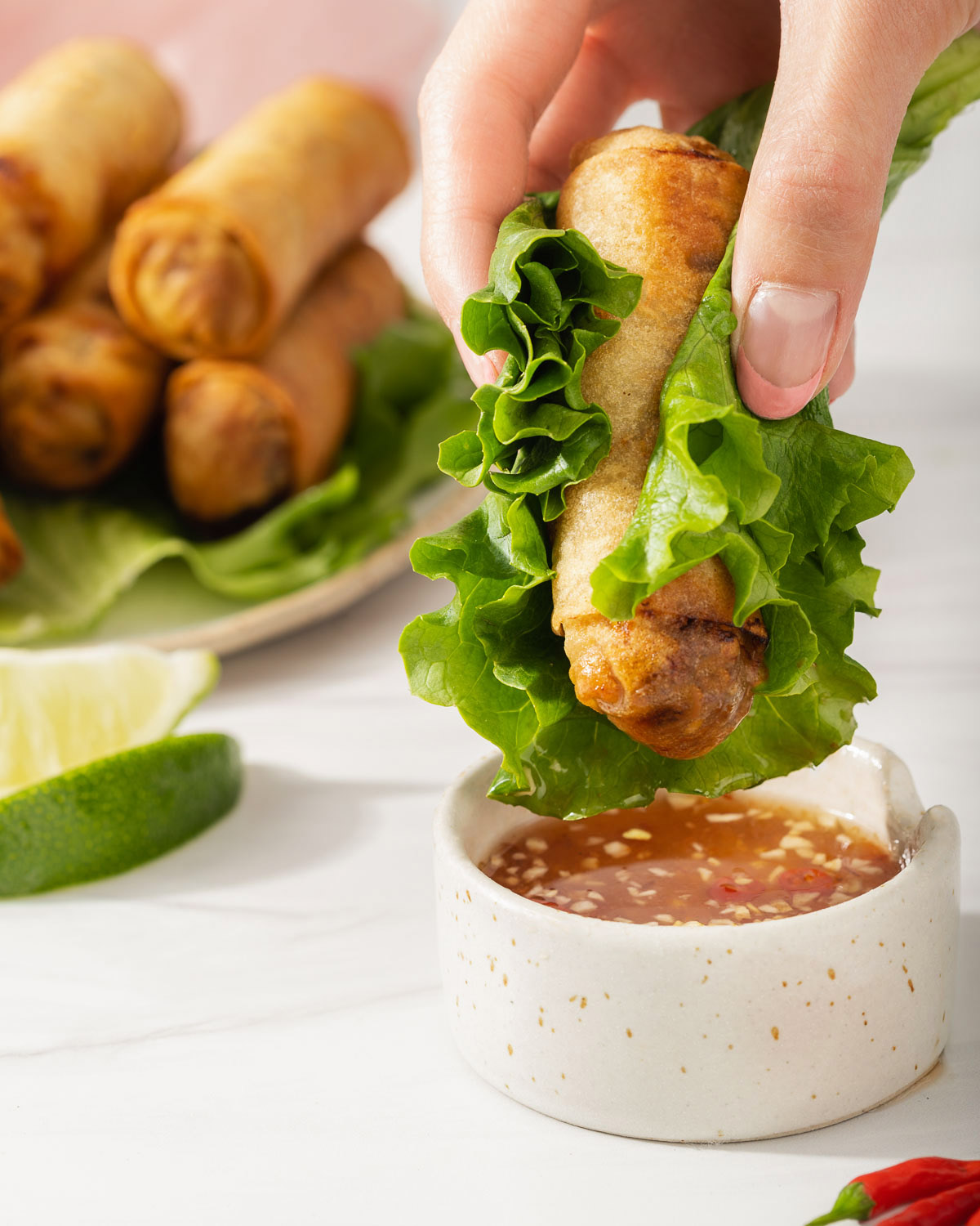 Dipping an egg roll wrapped in lettuce into a small bowl of nuoc cham dipping sauce.