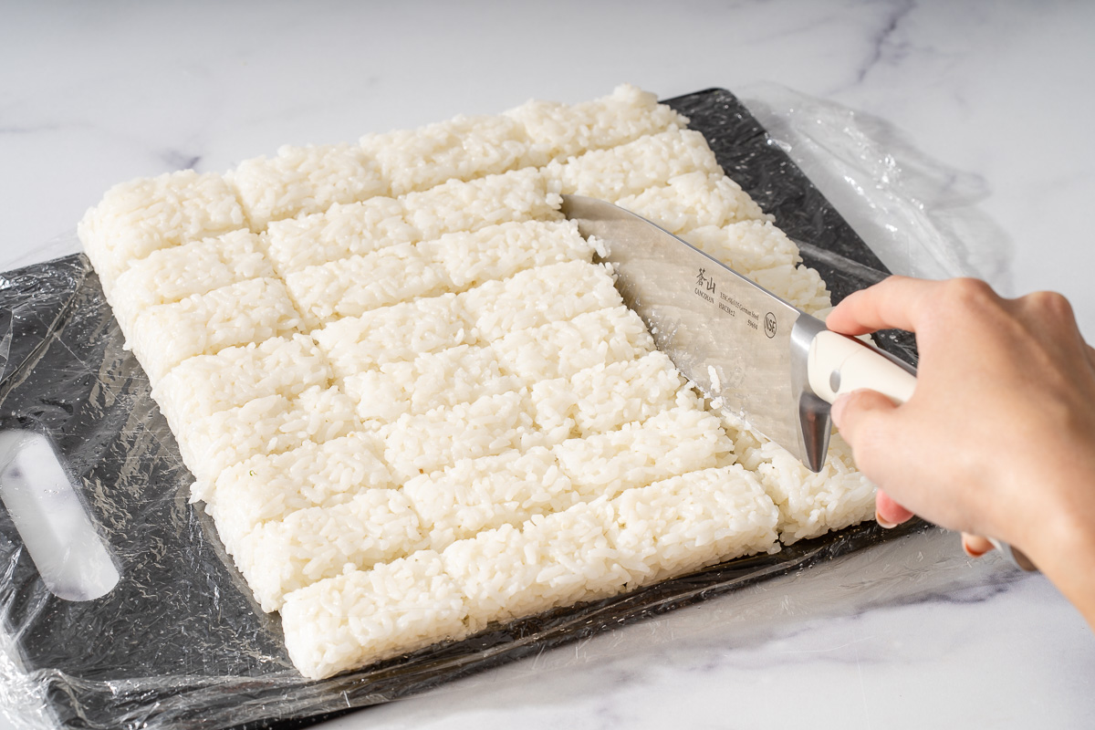 Slicing a block of cooled rice into bite sized rectangle pieces.