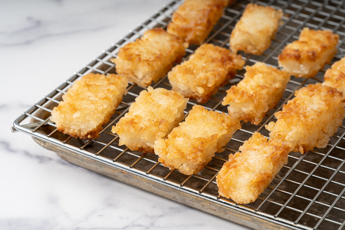 Fried rectangular crispy rice resting on a drying rack topped baking tray.